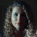 lexie, a woman wearing eye makeup red lipstick and has long curly blonde hair